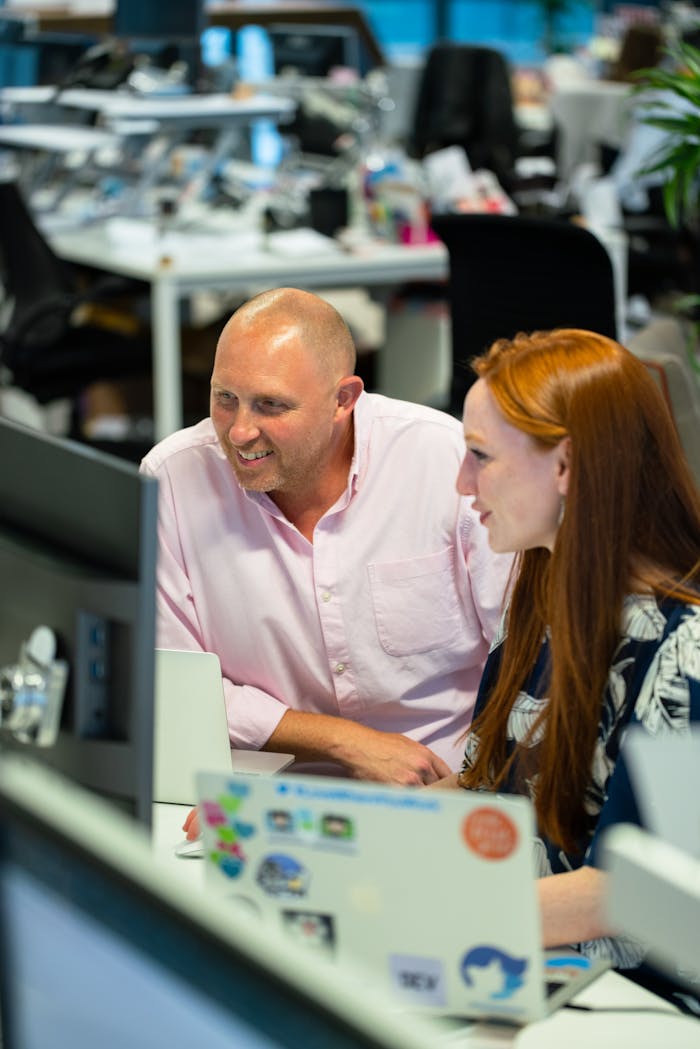 Two colleagues collaborating at a desk in a modern office environment, smiling and engaged.
